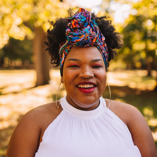 black woman wearing colorful head wrap outside with trees behind her