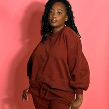 Load image into Gallery viewer, Black smiling girl in cinnamon colored jogger set standing in front of a pink background.
