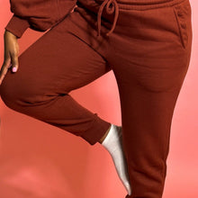 Load image into Gallery viewer, Black girl in cinnamon colored jogger set standing in front of a pink background.
