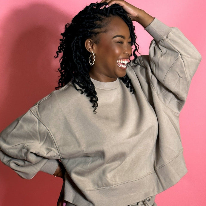 black girl smiling and wearing oatmeal colored joggers in front of a pink background.