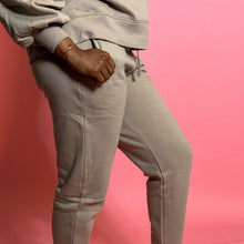 Load image into Gallery viewer, black girl smiling and wearing oatmeal colored joggers in front of a pink background.
