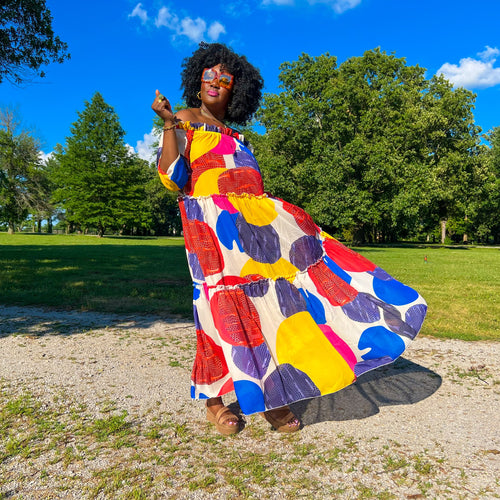 black woman with afro outside in park wearing an off the shoulder colorful mixed print maxi dress